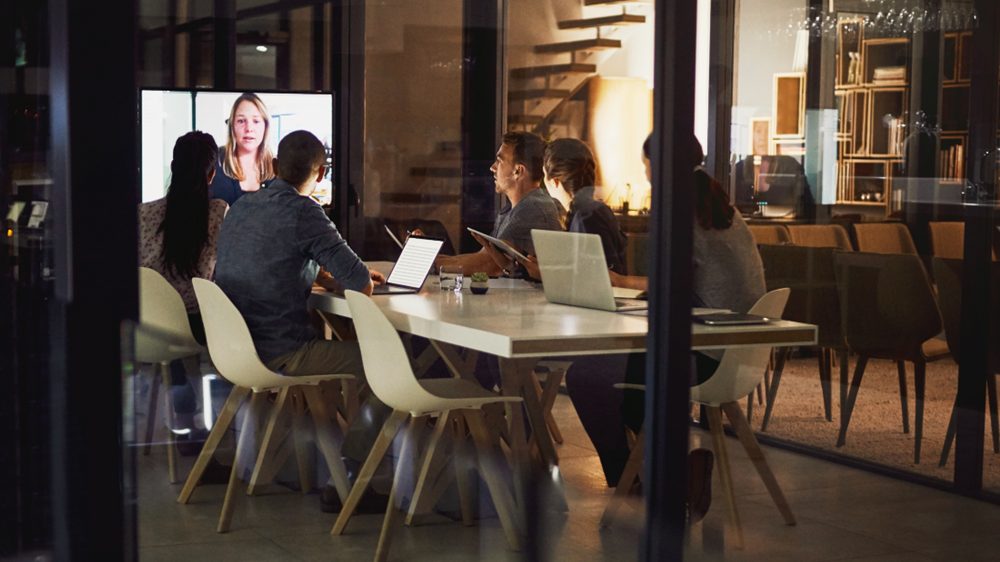 An executive team in a glass-walled conference room, working late