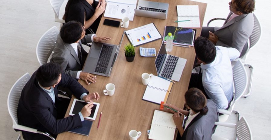 A working session seen from above — laptops, charts and notebooks across a table